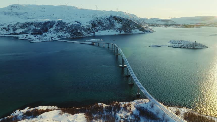 A huge bridge that crosses a vast amount of water in an arctic region with hills covered in snow