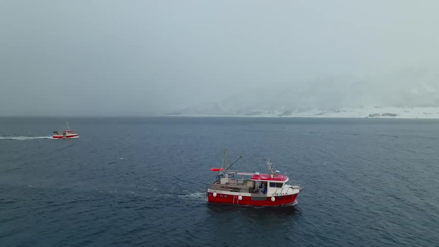 Boats navigating in the ocean with snow on the shores of the sea