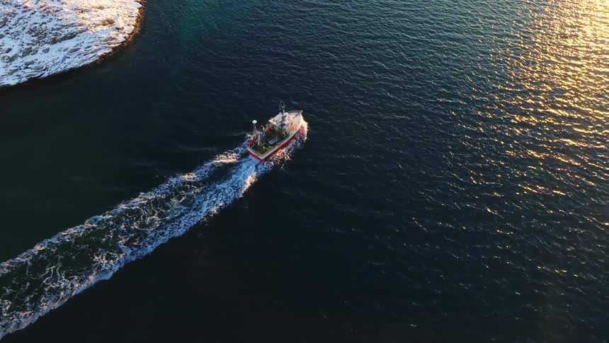 Aerial view of a boat sailing near the coast at sunset