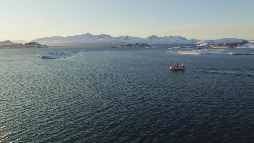 Aerial of a small boat floating on top of a large body of water at sunset