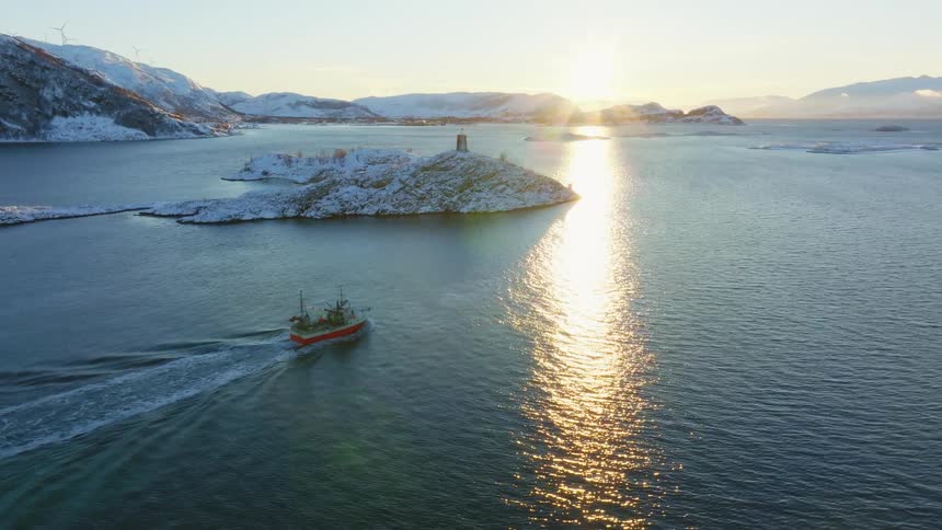 Commercial boat sailing in the sea with snowcovered mountains in the background at sunrise