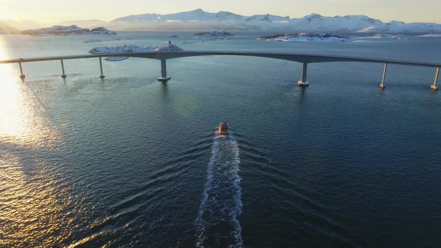 Aerial view of a boat approaching a bridge at sunset