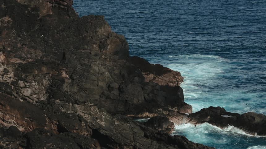 Aerial of ocean waves splashing against a rocky coastline