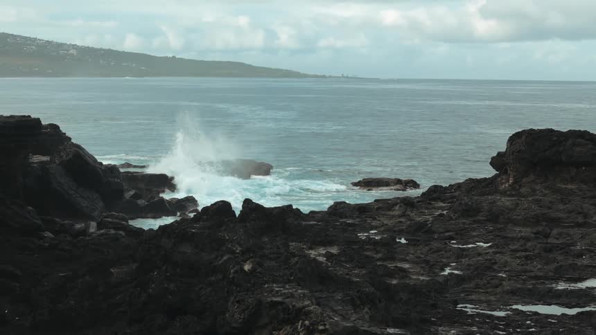 Sea waves breaking on the coast that is full of dark rocks