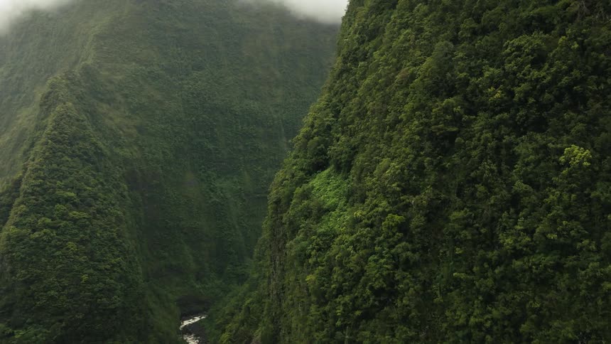 Aerial of a steep mountain range and a stream in a tropical area