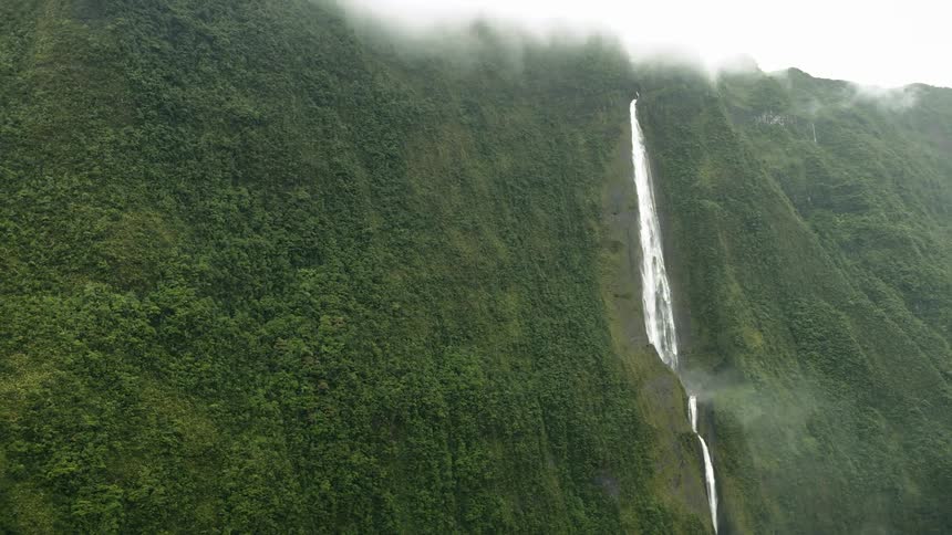 Aerial panorama on a cloudy day with a large forested mountain and a waterfall