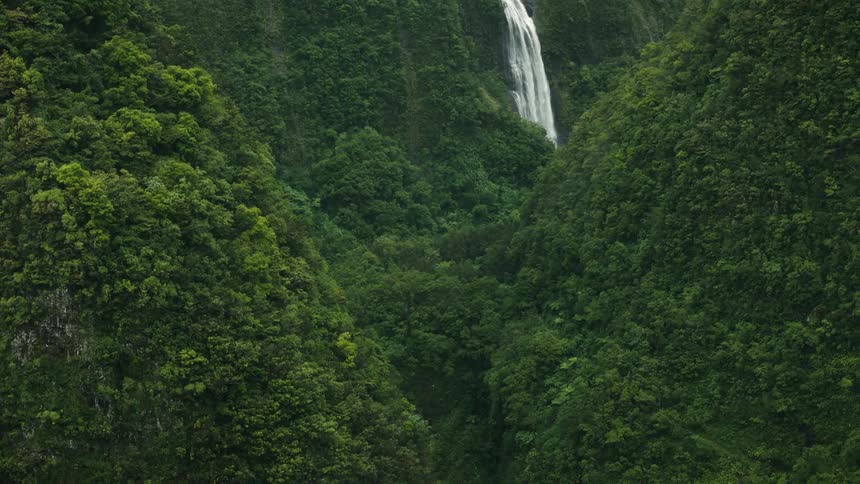 The waterfall pours off the green mountains