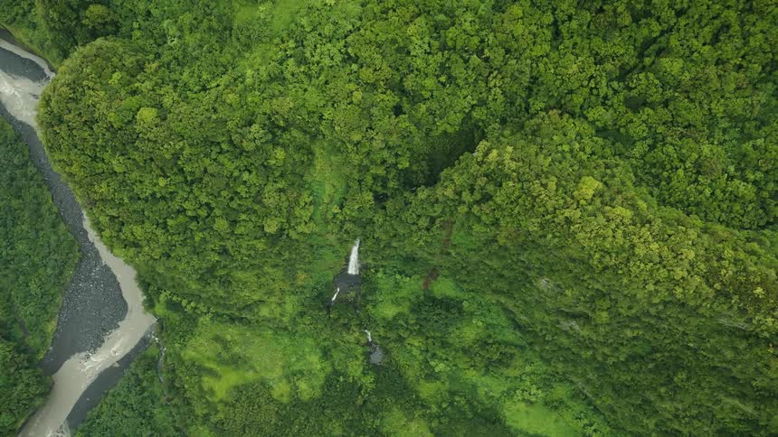 Aerial scenery of a forested mountain range with a waterfall on a flowing river