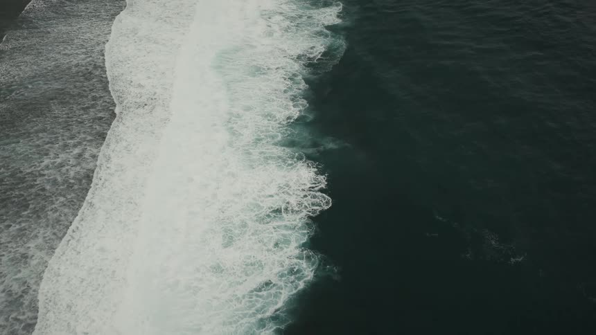 Small waves breaking on the beach and forming foam in the greenish water