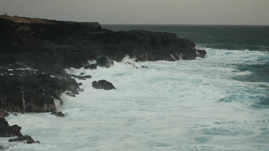 Aerial panorama of foamy sea waves crashing on coastal rocks on a cloudy day