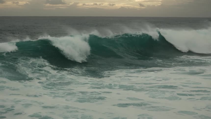Large wave foams while flowing across ocean on a cloudy day