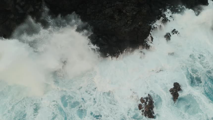 Aerial of ocean waves crashing against a rocky coastline