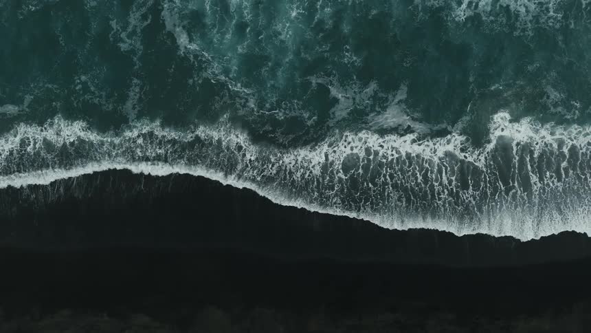 Aerial landscape of sea waves hitting the shore of a black sand