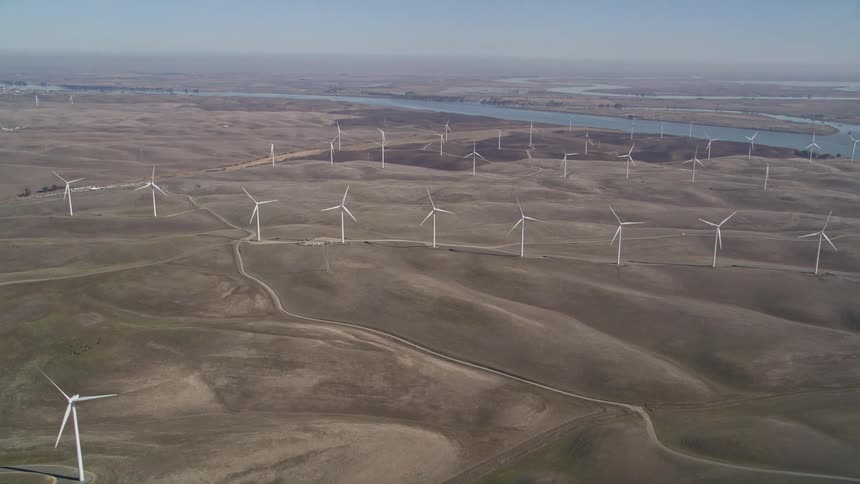 Aerial panorama of wind energy platforms and engines in natural fields on the edge of a river