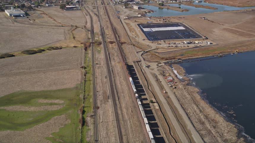 A train moves down tracks near bodies of water and a small town