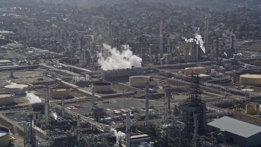 An aerial view of a factory with a building releasing a lot of white smoke