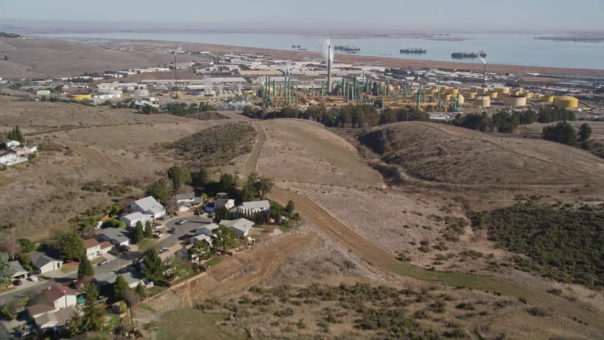 An aerial view of a residential area of a small town and in the background there is a large industry close to the sea