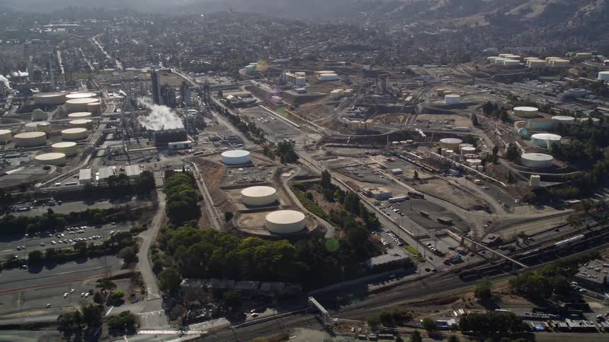 Aerial view of an industrial complex with storage tanks and an urban city on the horizon next to mountains