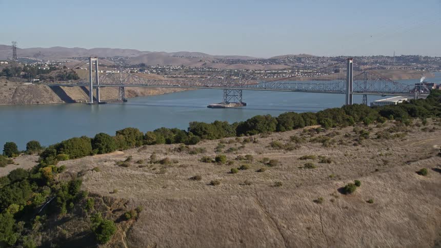 A small city with a bridge over water sits beyond a hill