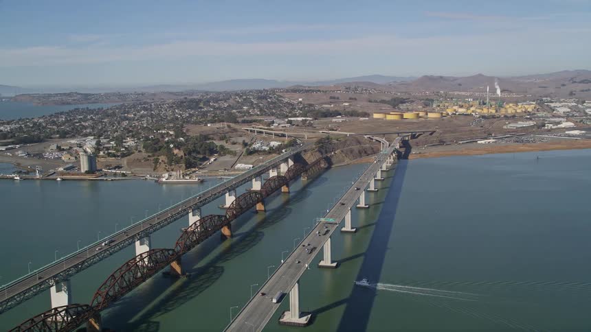 Aerial panorama of three bridges over the sea with vehicle and train traffic connecting urban cities with mountain silhouettes on the horizon