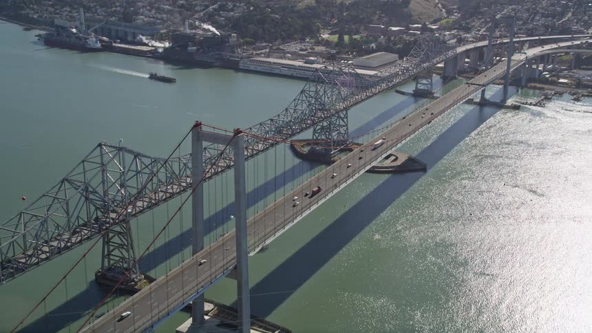 An aerial view of a bridge that goes over a bay and there is a huge ship parked in the water