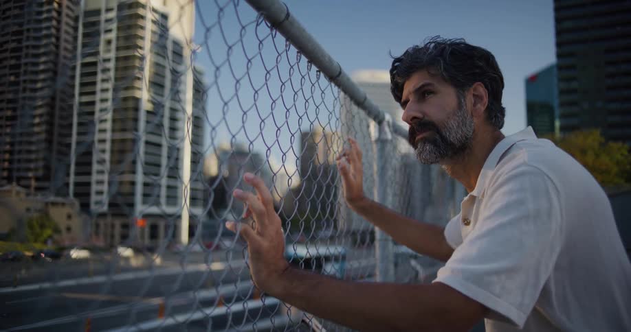 A man leans against a fence staring at a big city