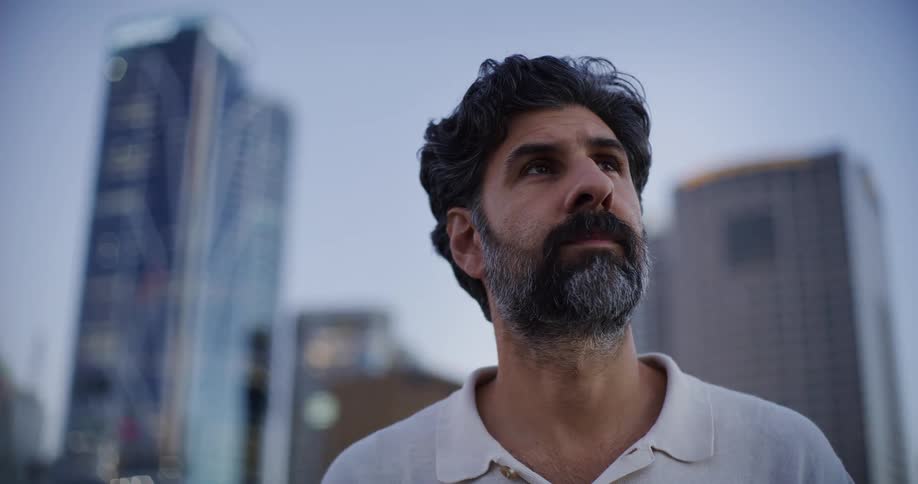 A bearded person looking at a city skyline during twilight