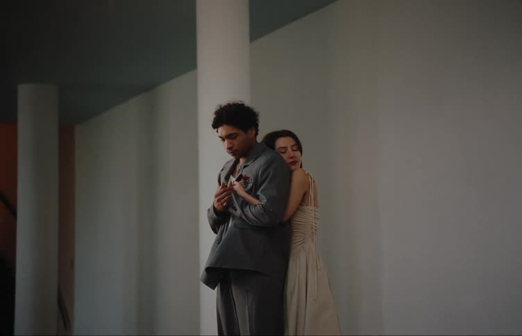 Woman in white dress affectionately hugging her boyfriend from behind while they are in the hallway of a building