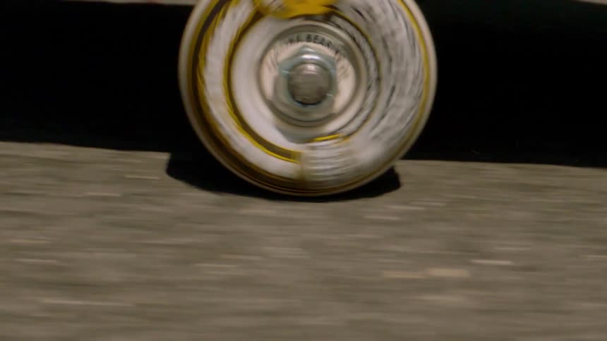 A white and yellow skateboard wheel is rolling on a rough ground