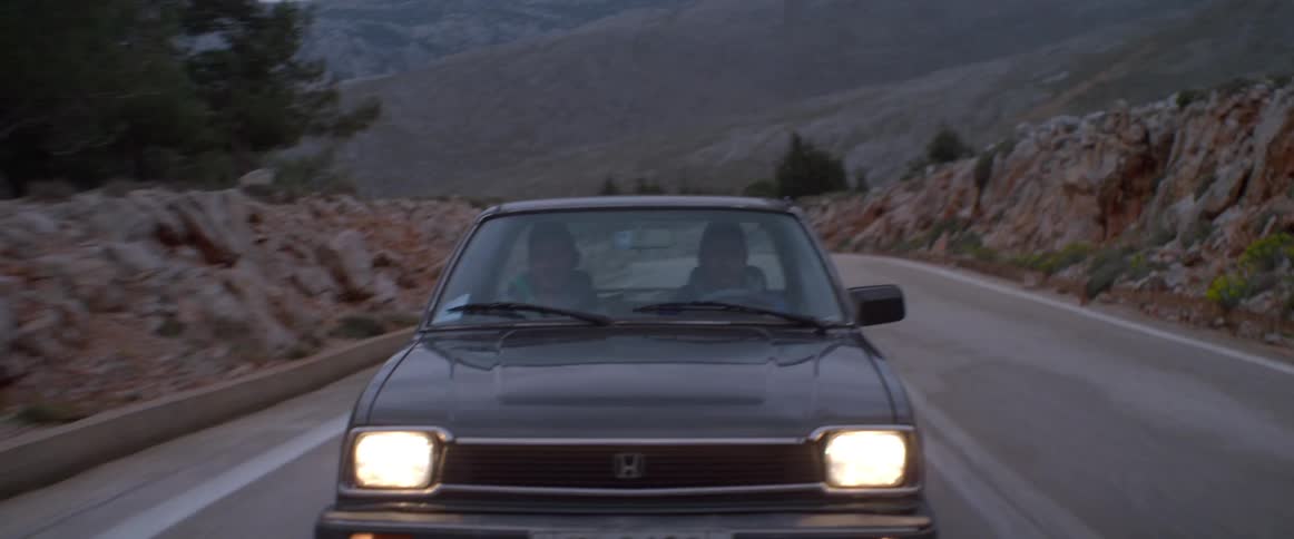 Two people ride in a blue car on an overcast day