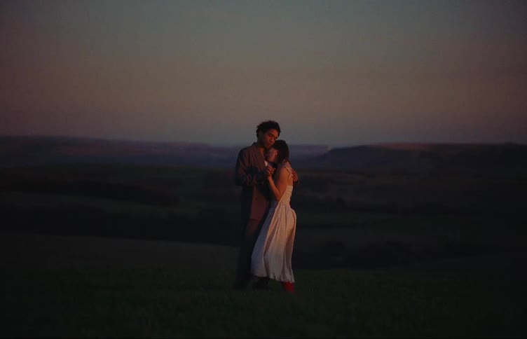 A man and a woman share a hug while standing on a grassy field