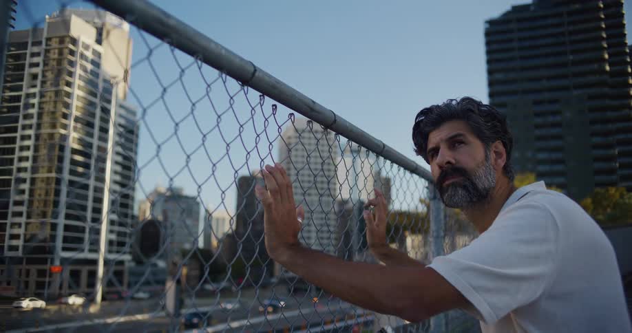 A man leans on a fence while looking around at a city