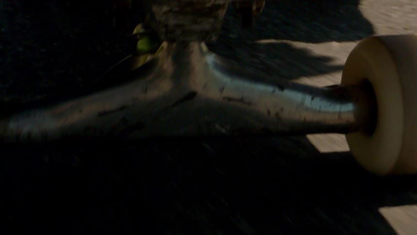 A skateboard passing over a ground with a rough texture and creating a shadow on the ground