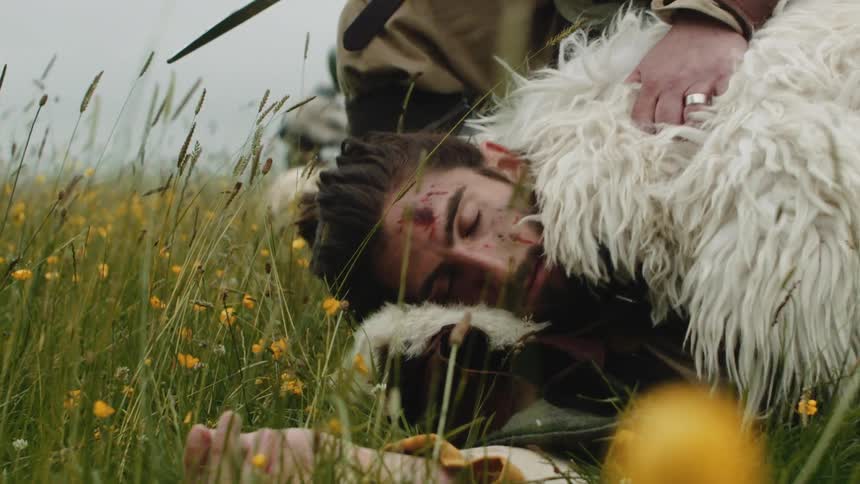 A medieval warrior wearing an animal skin lays in the grass wounded
