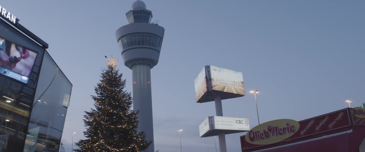 Airport control tower at dusk with a lit christmas tree and advertisements on the surrounding buildings