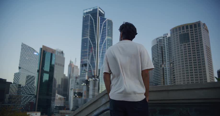 A bearded man in a casual collared shirt stands before a city skyline