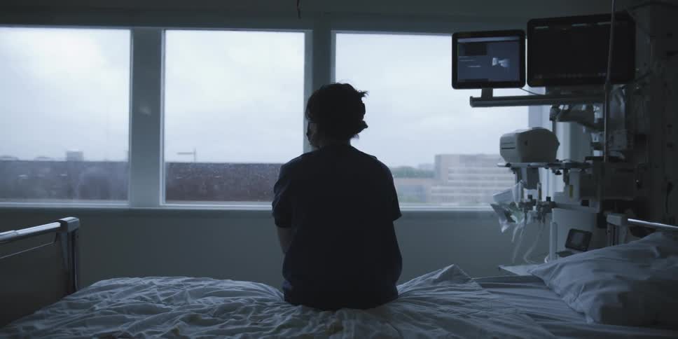A silhouette of a person sitting in a hospital room gazing out of the window