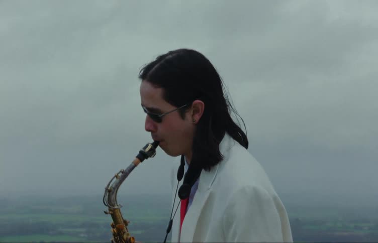 A man wearing a white blazer plays the saxophone outdoors