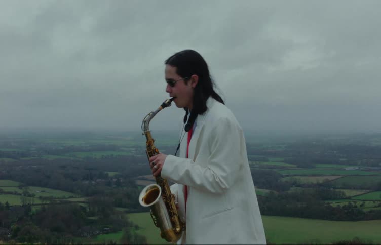 A person in a white coat playing a saxophone with a scenic landscape