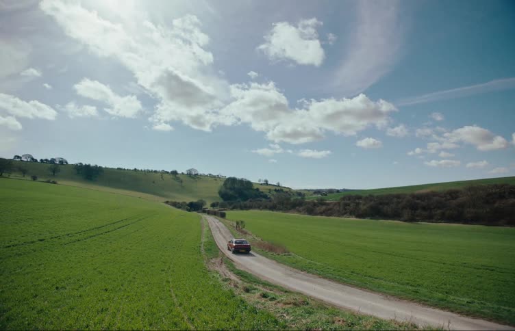 Red car driving down a narrow road in a rural area