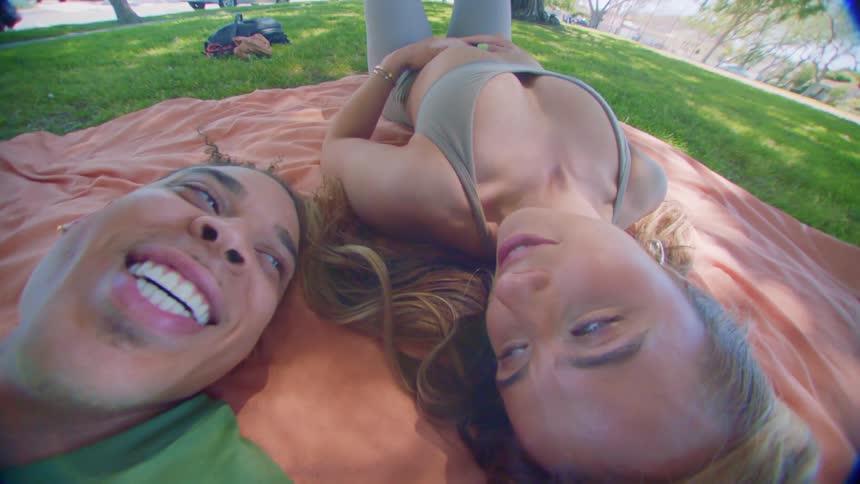 Couple lying on a blanket on the grass smile at each other while talking