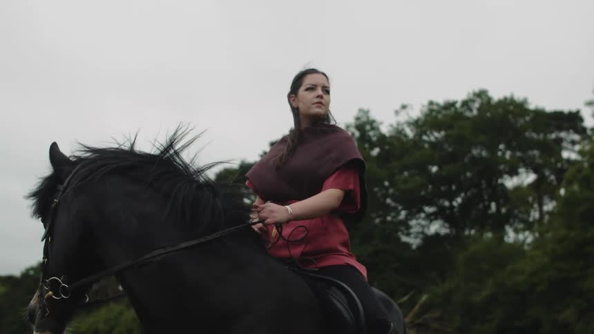 A woman wearing medieval garb sits on a horse