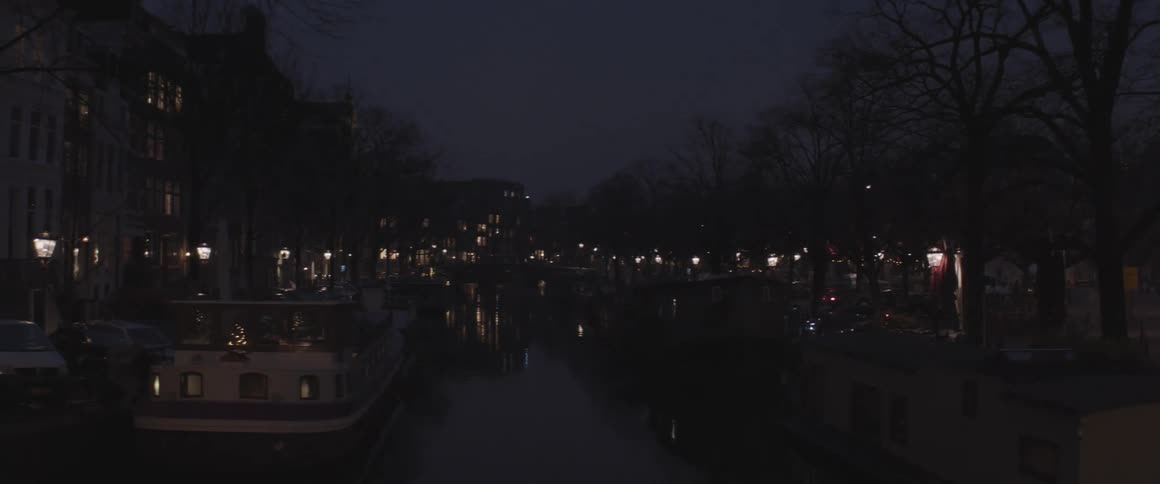 Boats line river reflecting apartment building at night during winter