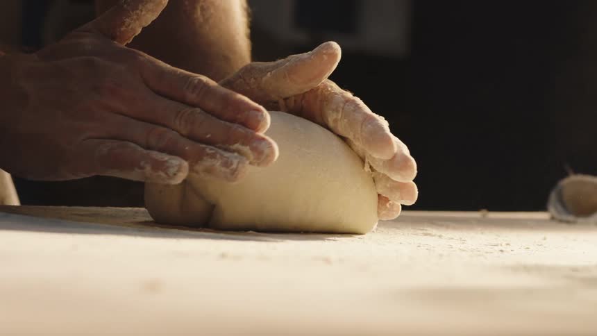 A worker kneads dough on a table