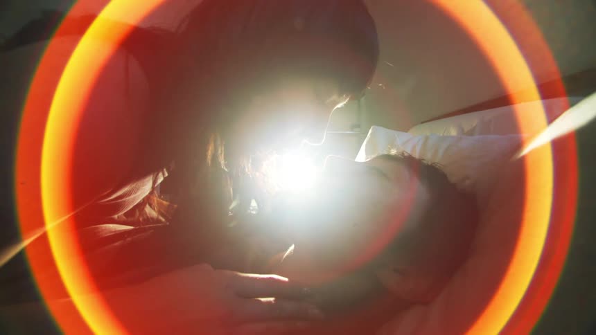 An asian couple kiss in bed and are surrounded by a circular lighting effect