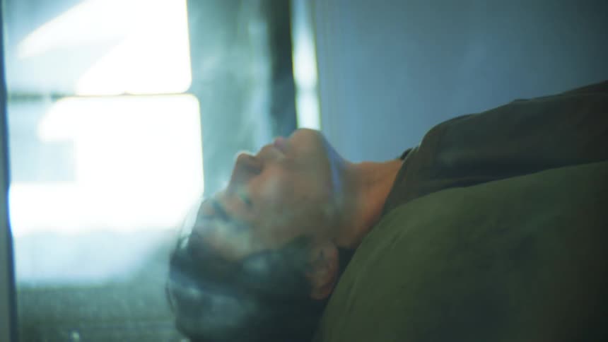 A woman folds a cloth while a man lies down on a bed