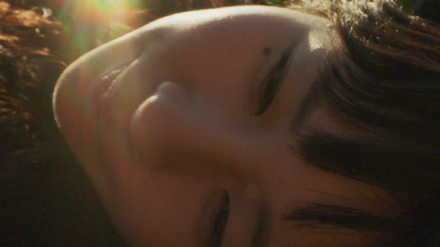Portrait of a young woman outdoors lying down with sunlight reflecting off her face