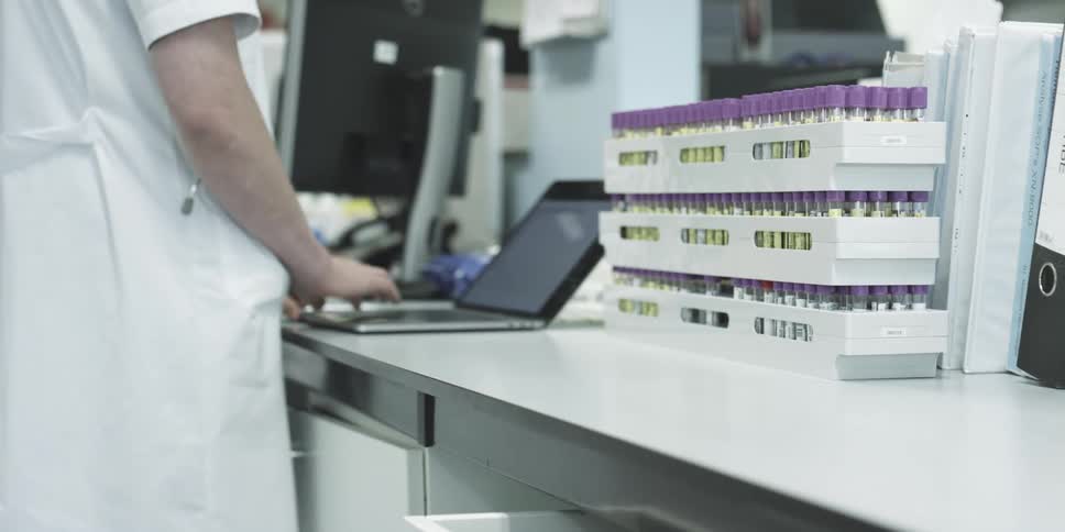 A lab employee types on a laptop computer while standing at a counter top