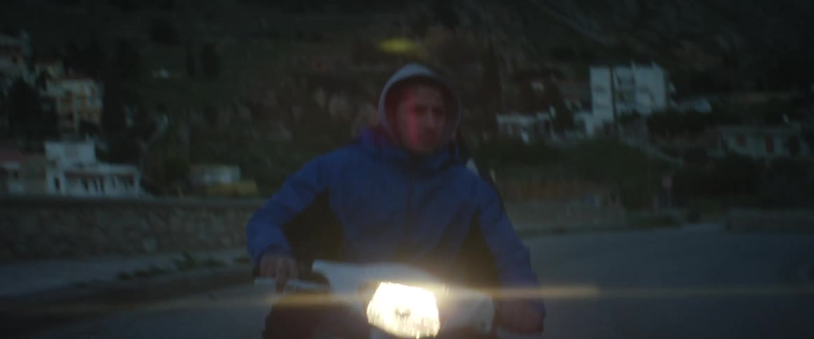 A man and a passenger ride a motorcycle up a winding road at night