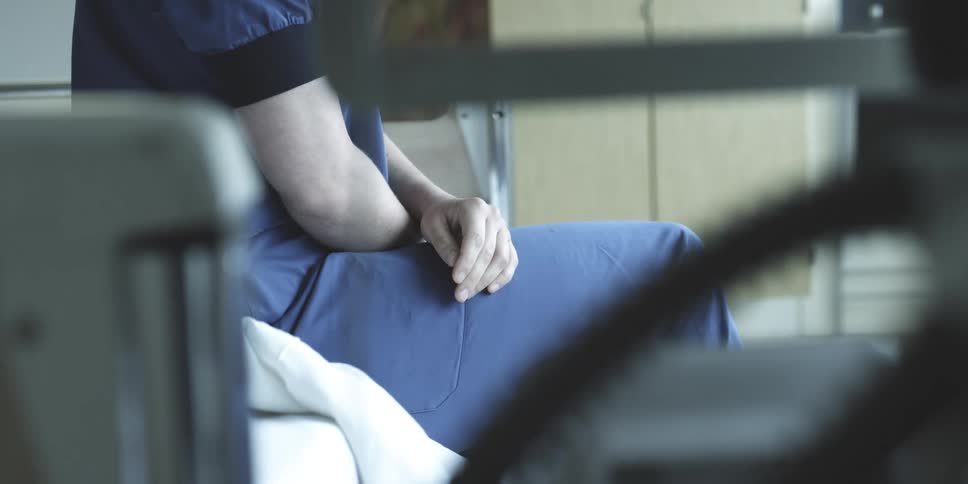 Healthcare professional in blue clothes sitting on a bed in a hospital